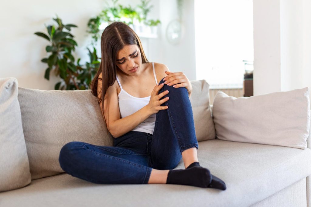 Woman holding the knee with pain on sofahealth care and medical concept
