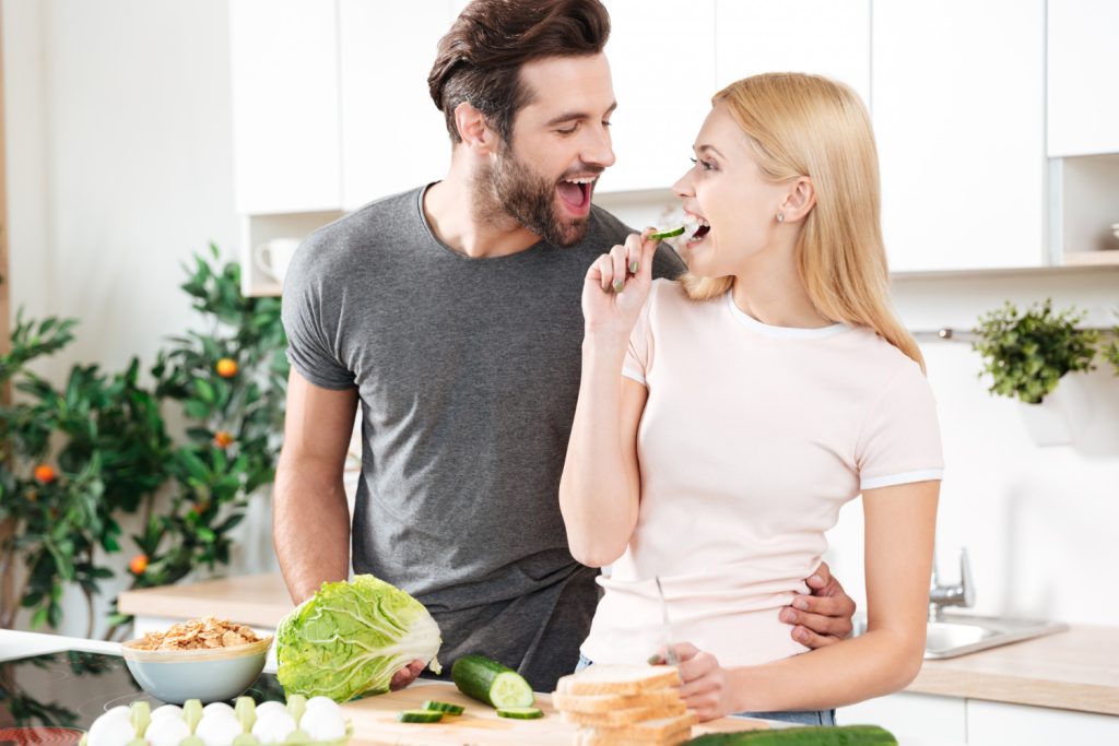 Funny young loving couple standing at kitchen and cooking
