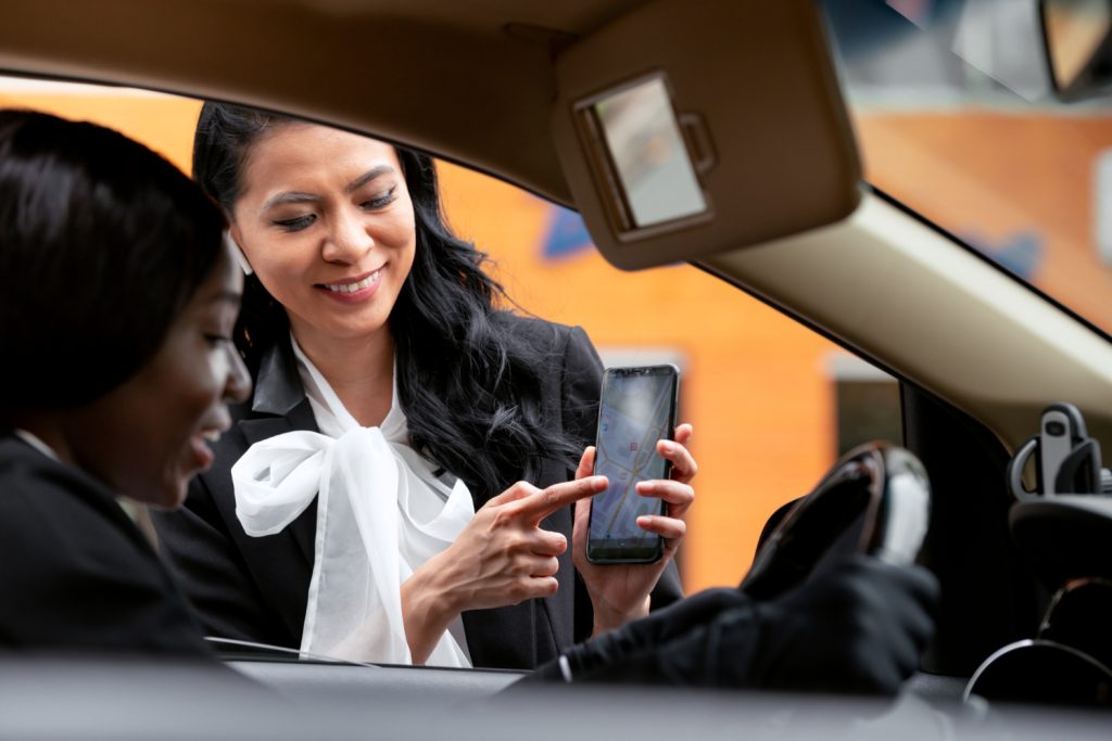 Businesswoman showing her smartphone app to the taxi driver with smile